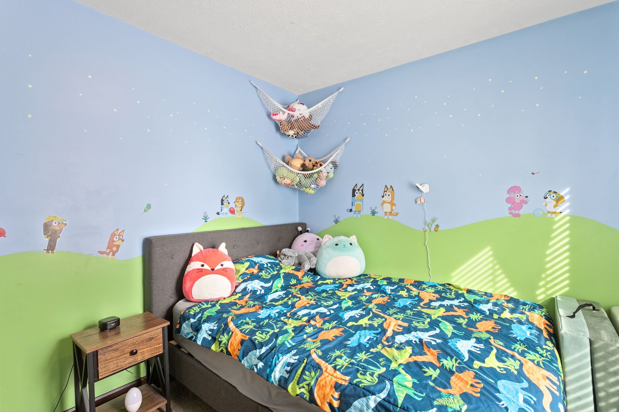 Children’s bedroom with cartoon wall mural, stuffed animals, and dinosaur bedding
