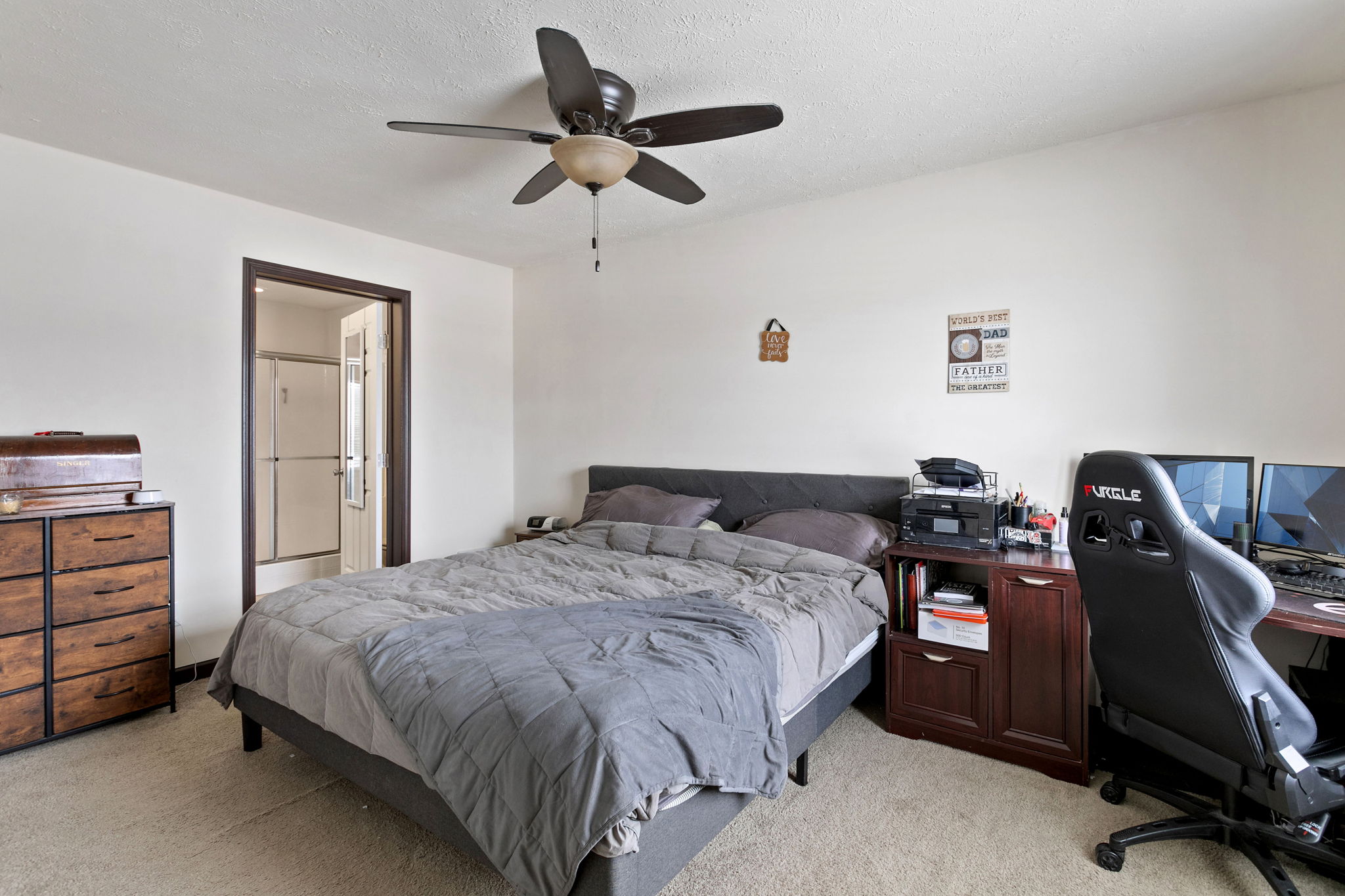 Alternate view of primary bedroom with ceiling fan, dresser, and doorway to bathroom