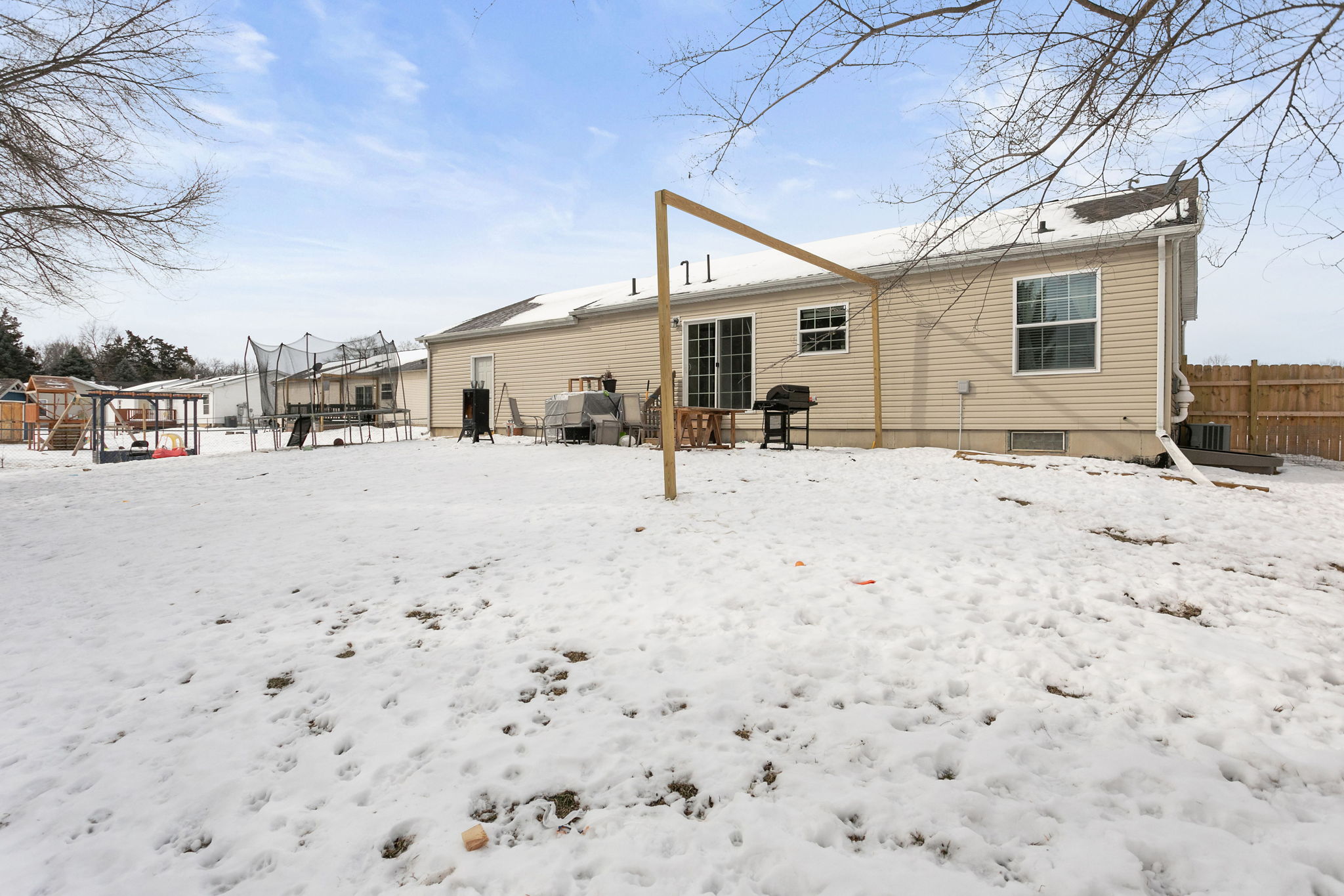Angled view of the backyard and house exterior, showing snow, grill, and trampoline.