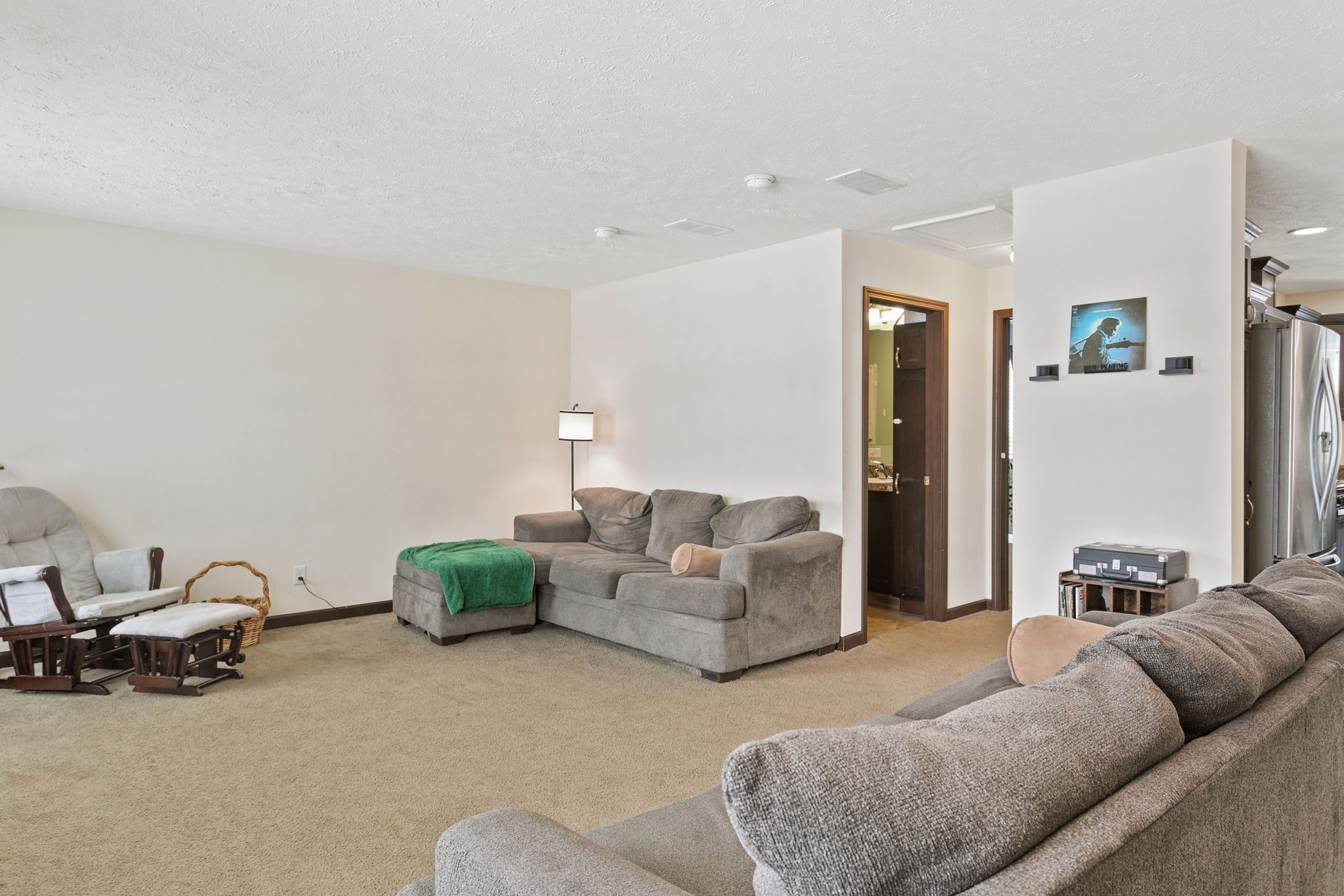 Living room featuring beige carpet, a gray sectional couch, and a floor lamp next to an open hallway.