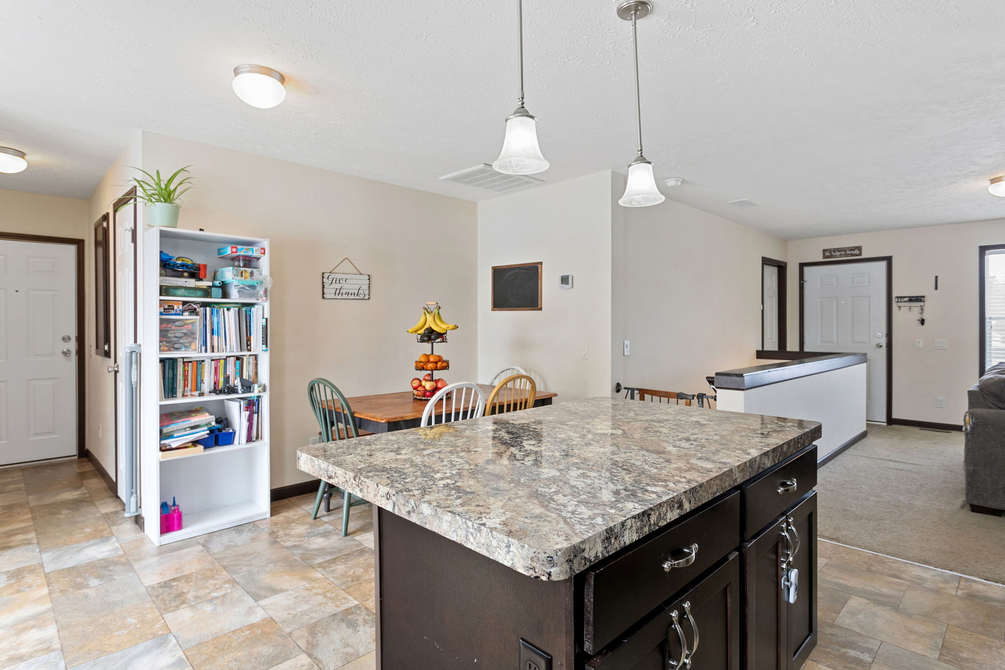 Kitchen and dining area with a granite island, tile flooring, and a bookshelf near the back door.