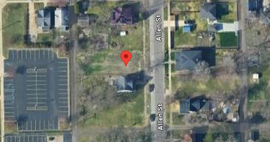 Aerial view of vacant residential lot on Allen St in South Bend, IN near parking lot and homes.