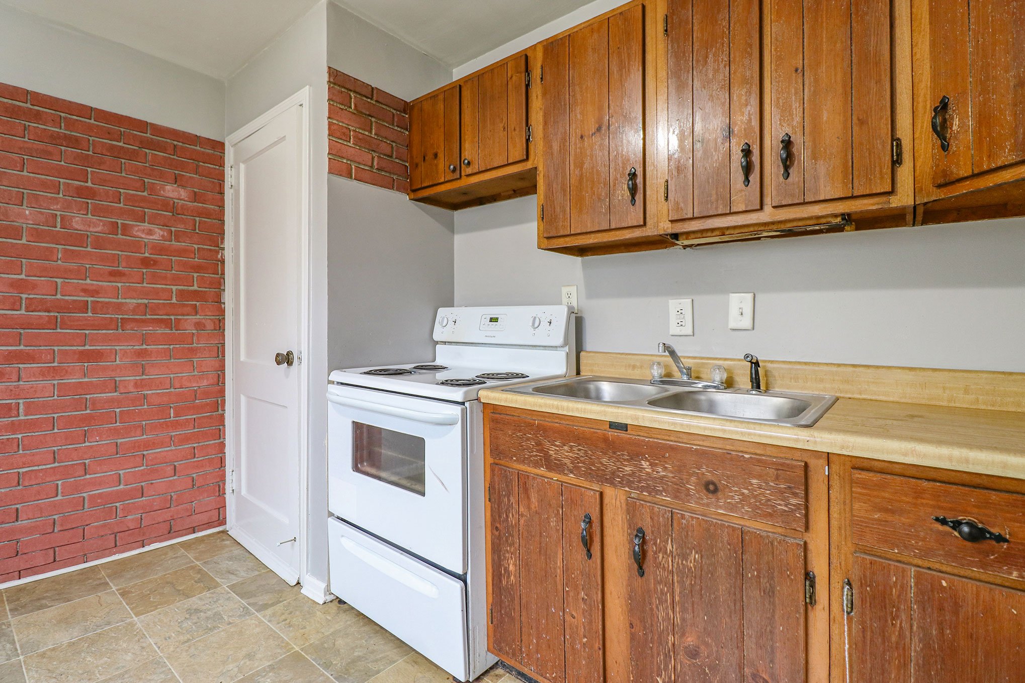 South Bend kitchen with vintage wood cabinets, electric stove, and red brick accent wall.