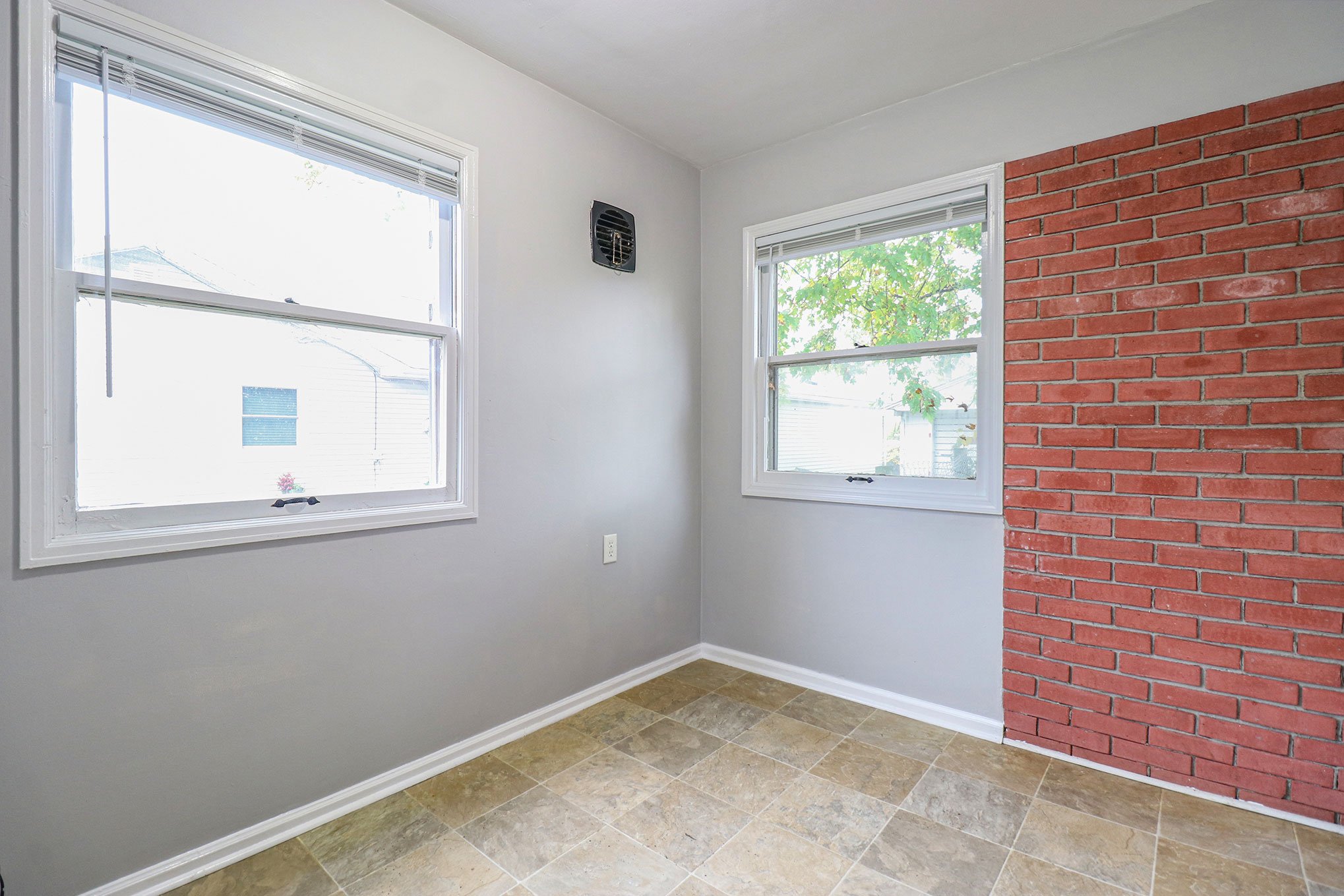 Bright dining nook with tiled floor, two large windows, and a red brick accent wall.