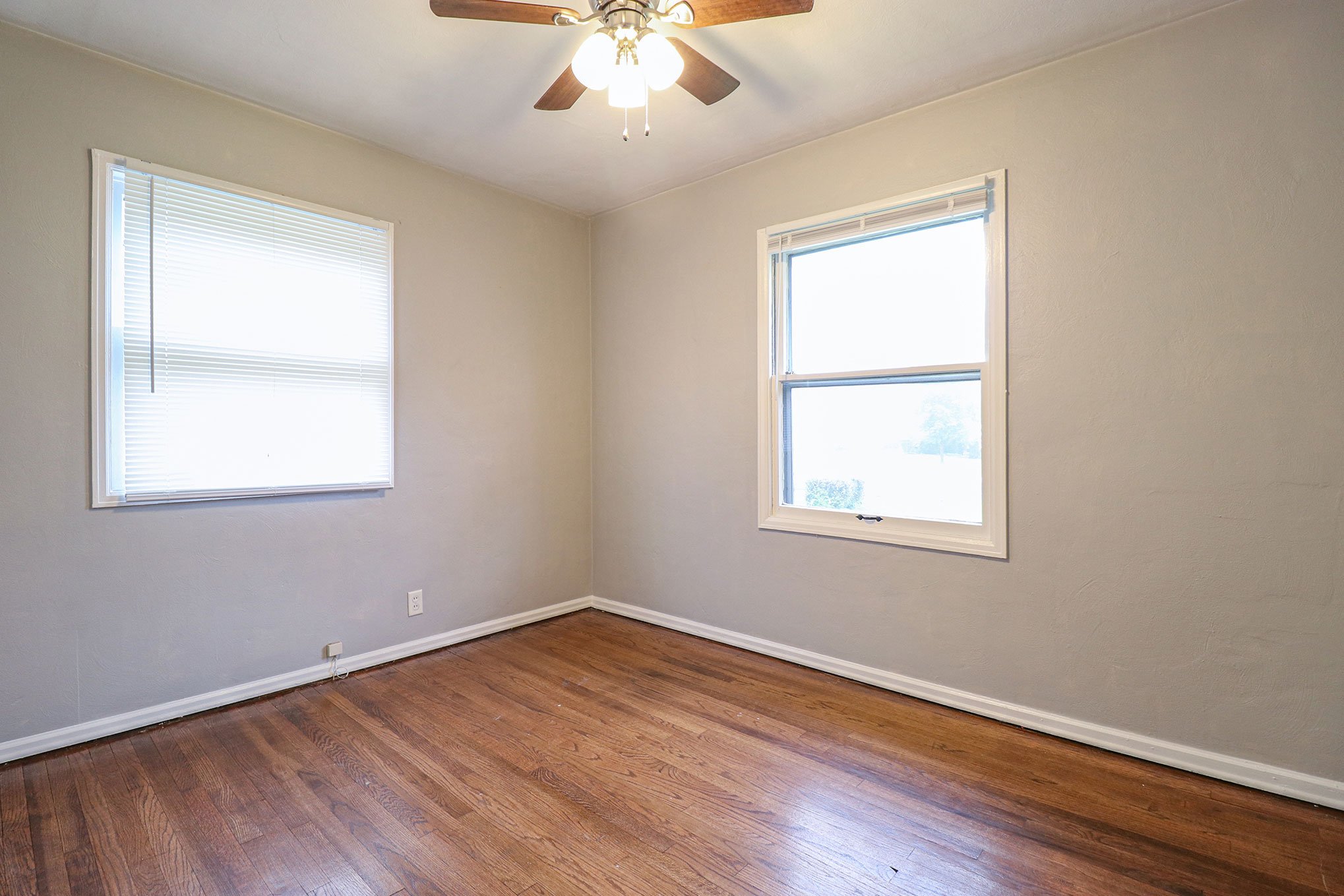 Small bedroom with hardwood floors, ceiling fan, and two windows bringing in natural light.