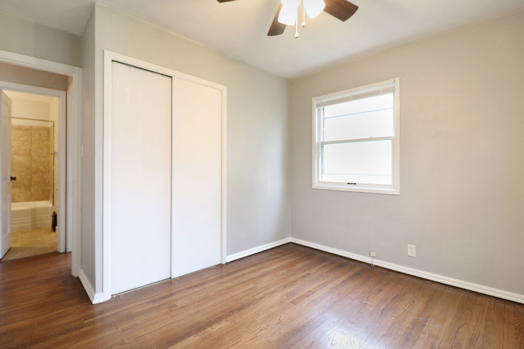 Bedroom with hardwood flooring, sliding closet doors, and a view into the hallway and bathroom.