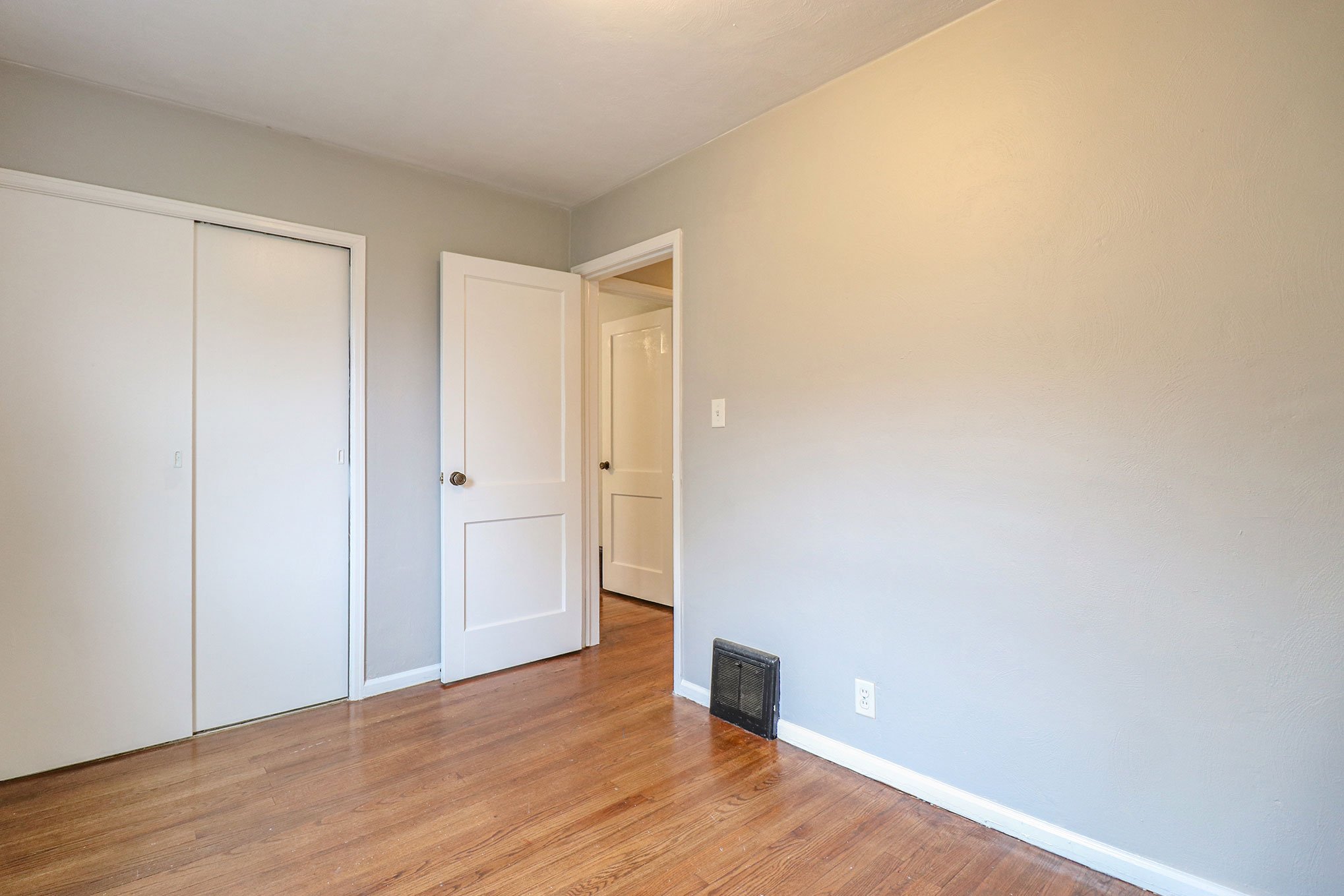 Bedroom interior with hardwood floors, gray walls, white closet doors, and open entry to hallway