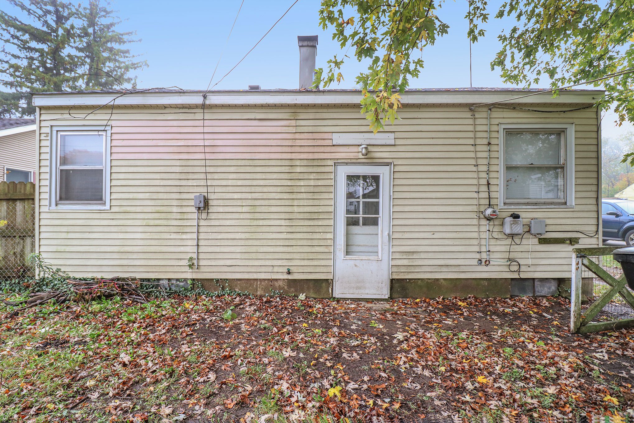 Rear exterior view of a small house with tan siding, two windows, and a white back door