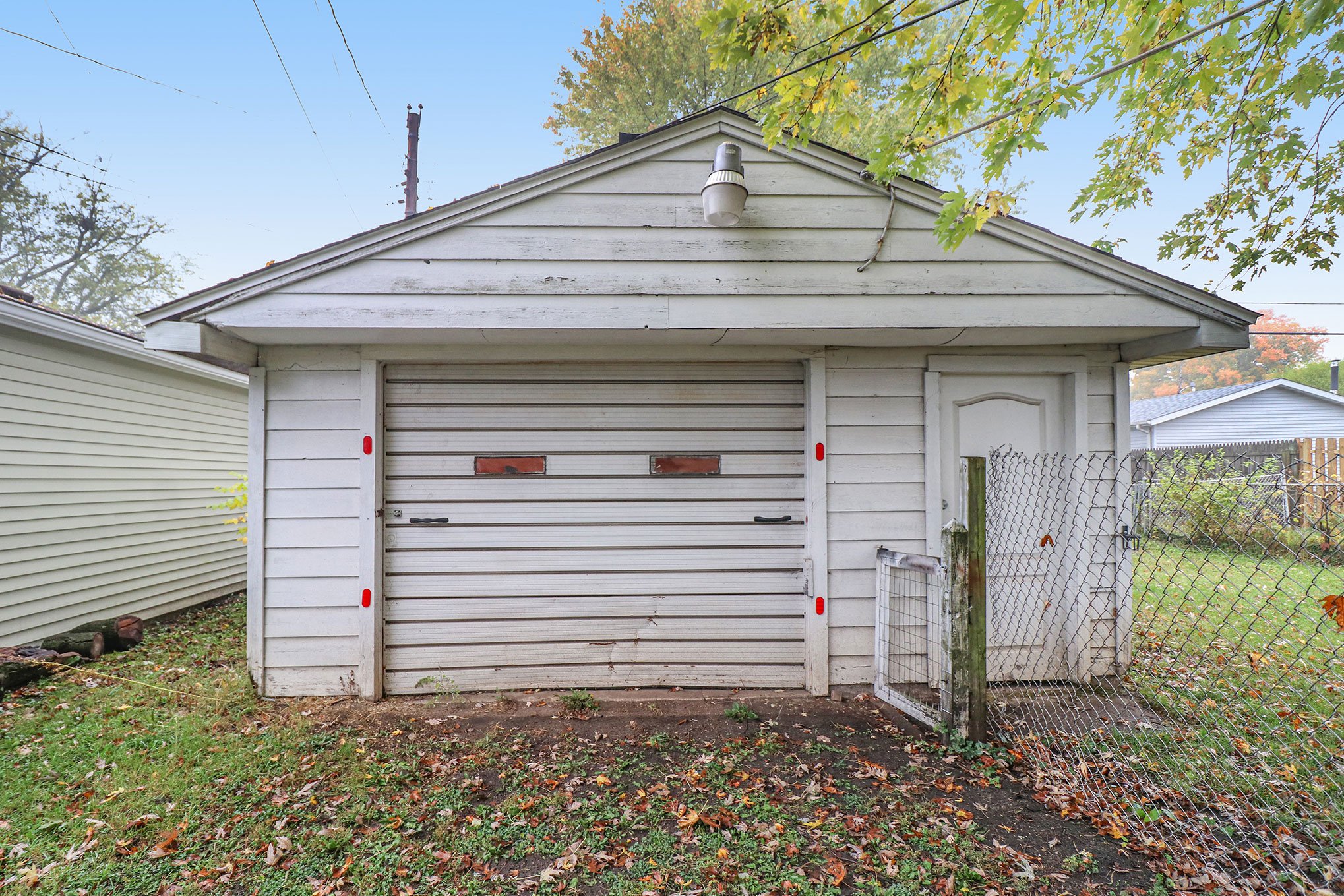 Detached white garage with overhead door, side entry door, and chain-link gate
