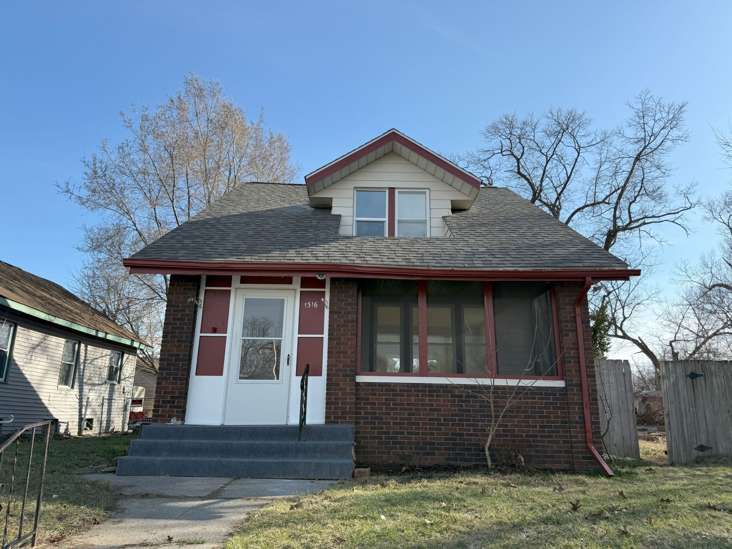 Two-story brick home with front porch and gabled roof in residential neighborhood