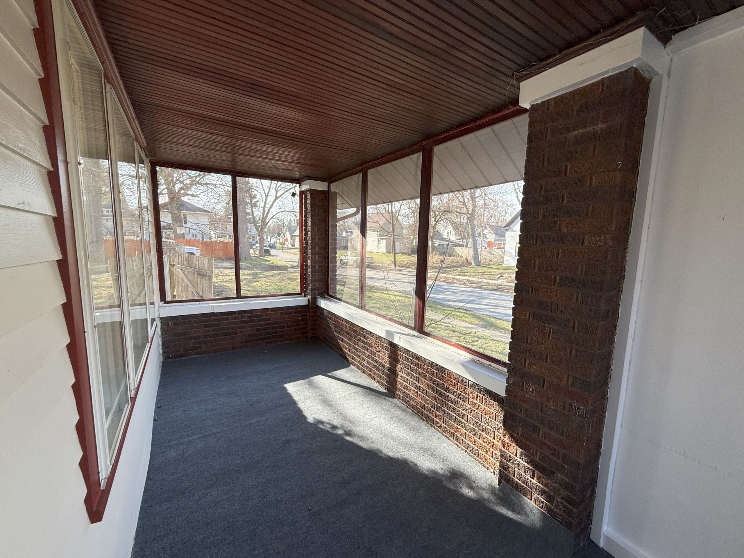 Enclosed front porch with brick accents and screened windows overlooking quiet street