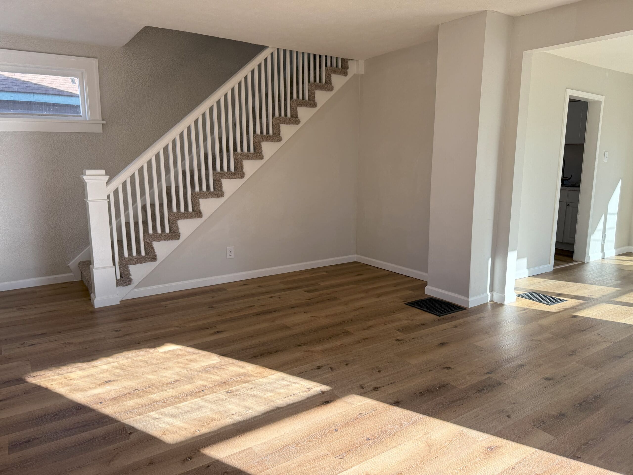 Spacious living room with wood flooring and carpeted staircase to upper level
