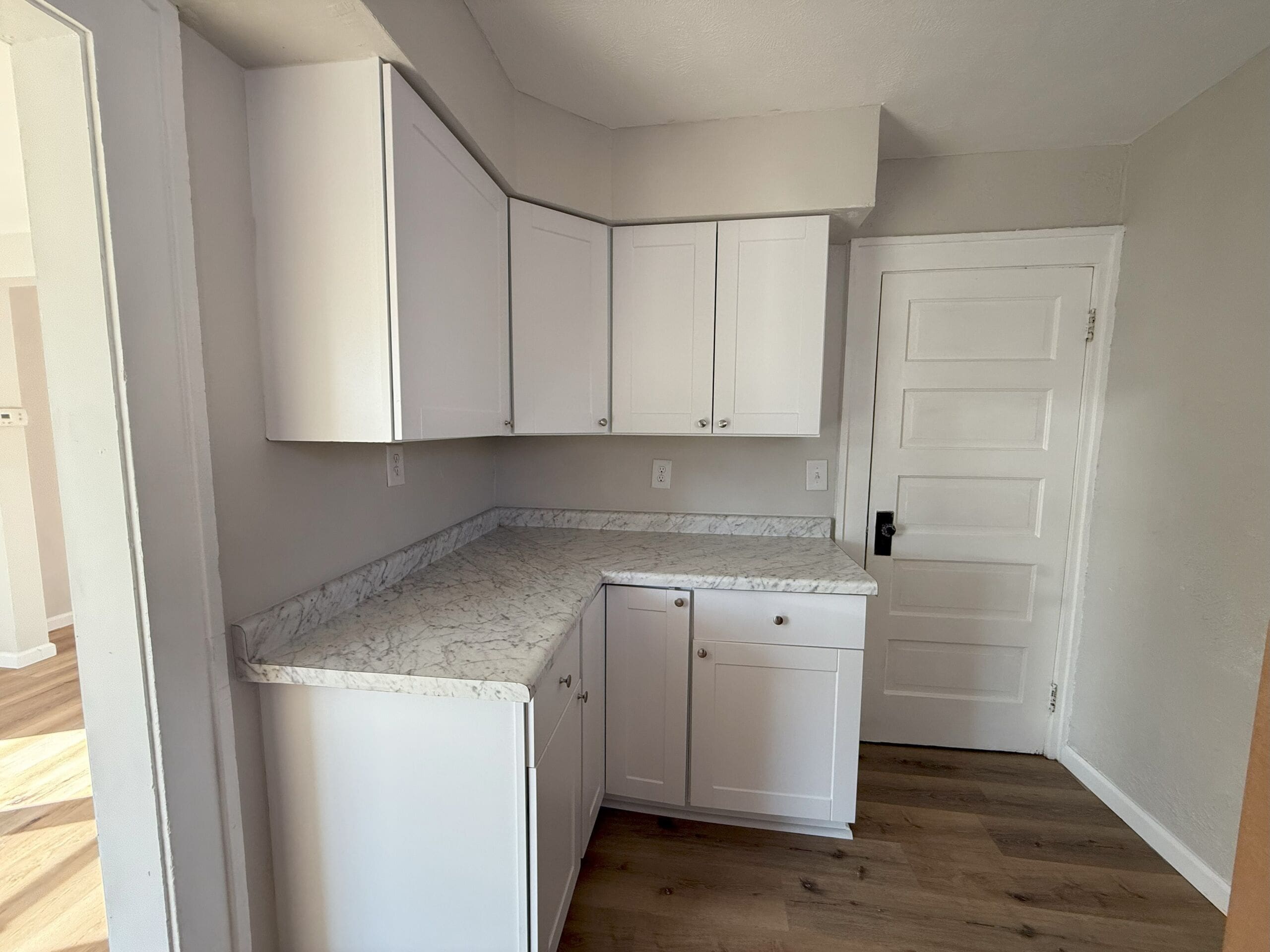 Modern kitchen with white cabinets, marble-look countertops, and wood flooring